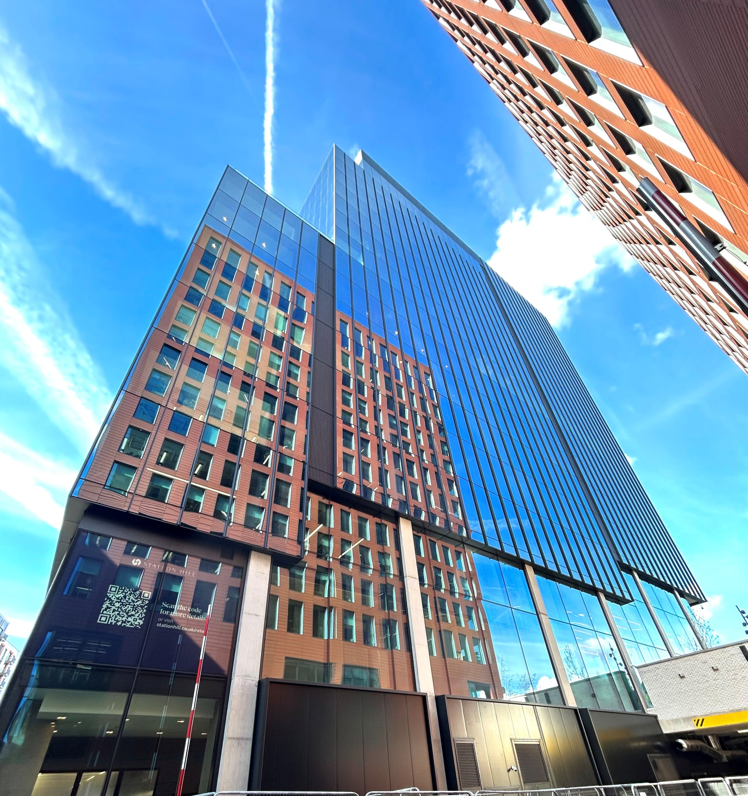 J M Partnership works on Landmark office building in the Centre of Reading. Commercial. “Landmark modern office building in the centre of Reading, featuring a glass and red-brick facade reflecting the blue sky and nearby structures.